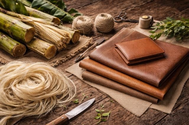 Raw banana fibres and finished brown vegan leather goods on a wooden surface
