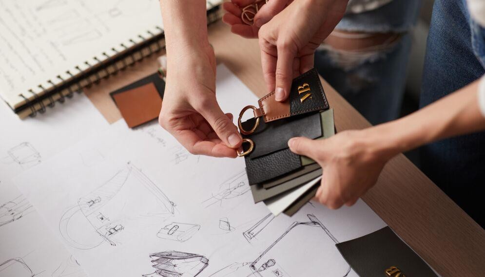 Hands holding vegan leather keychains over design sketches